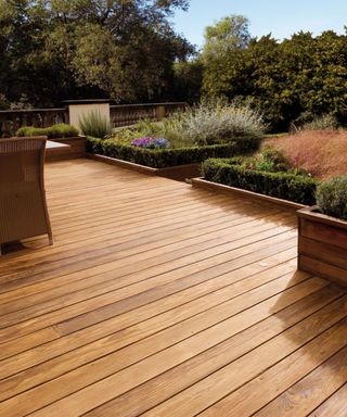 A large, light stained decking with a outdoor chair and expansive garden on the right
