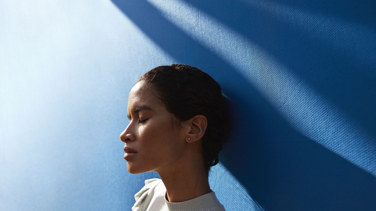 woman leaning against a blue wall with shadows