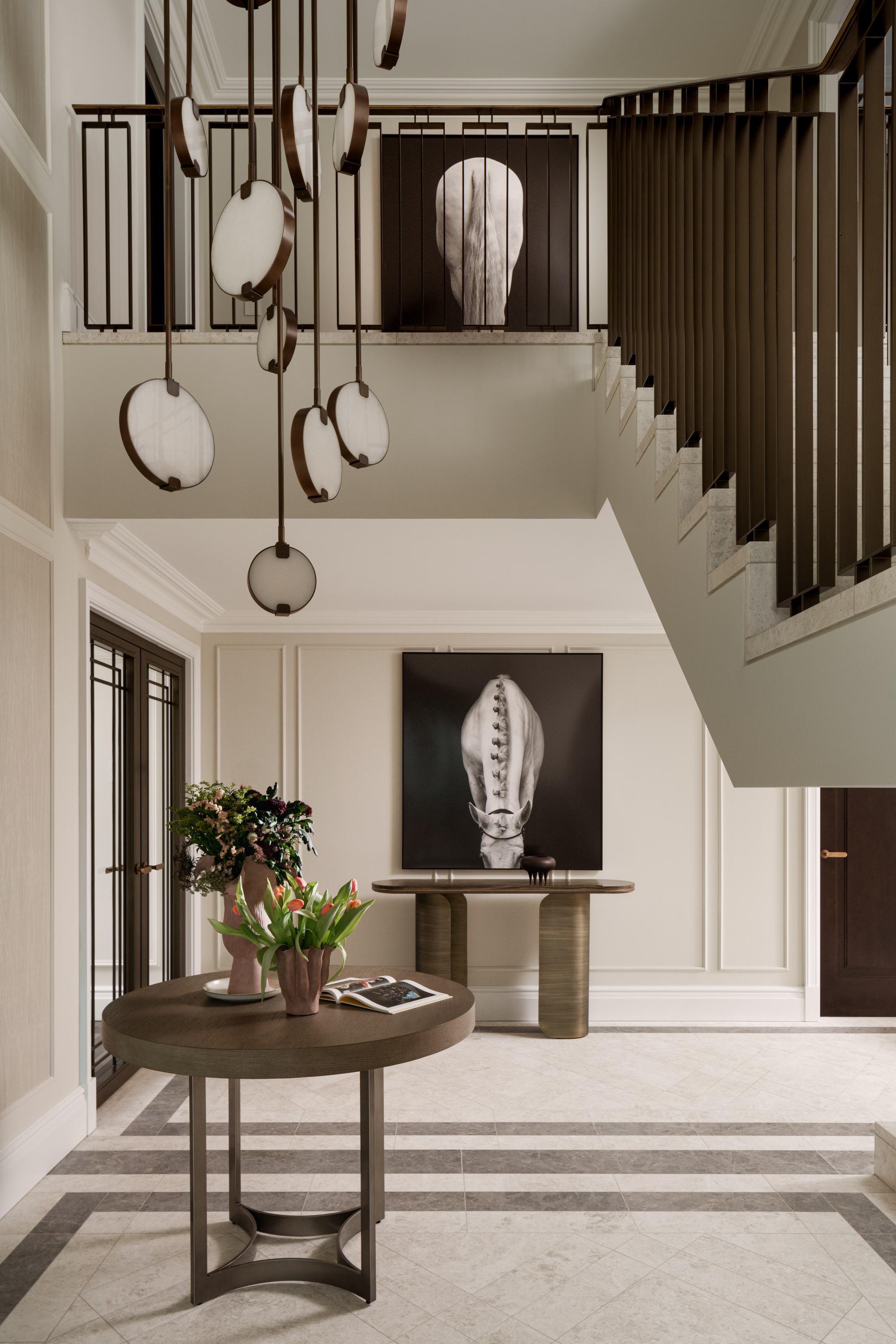 expansive entryway with round table styled with flowers and books, a console table under a work of art, tiled floors, and a staircase with a void with a large pendant light hanging down