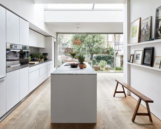White kitchen with kitchen island, open shelving, handleless cabinets and sliding glass doors leading out onto a garden.