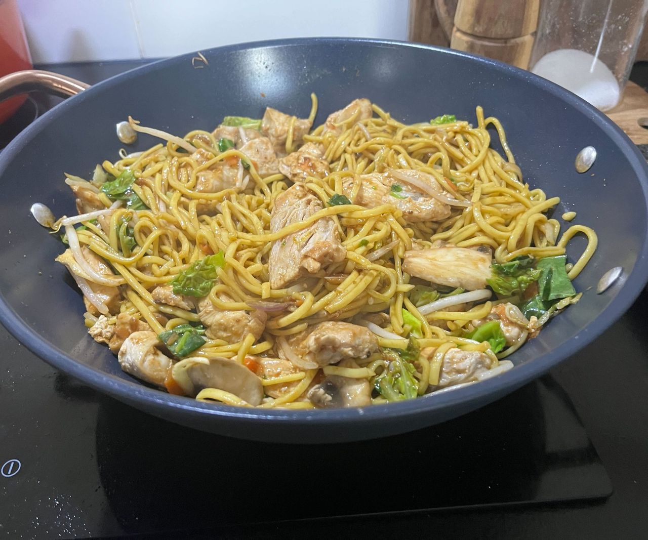 A chicken stir fry with egg noodles in a blue ceramic wok.
