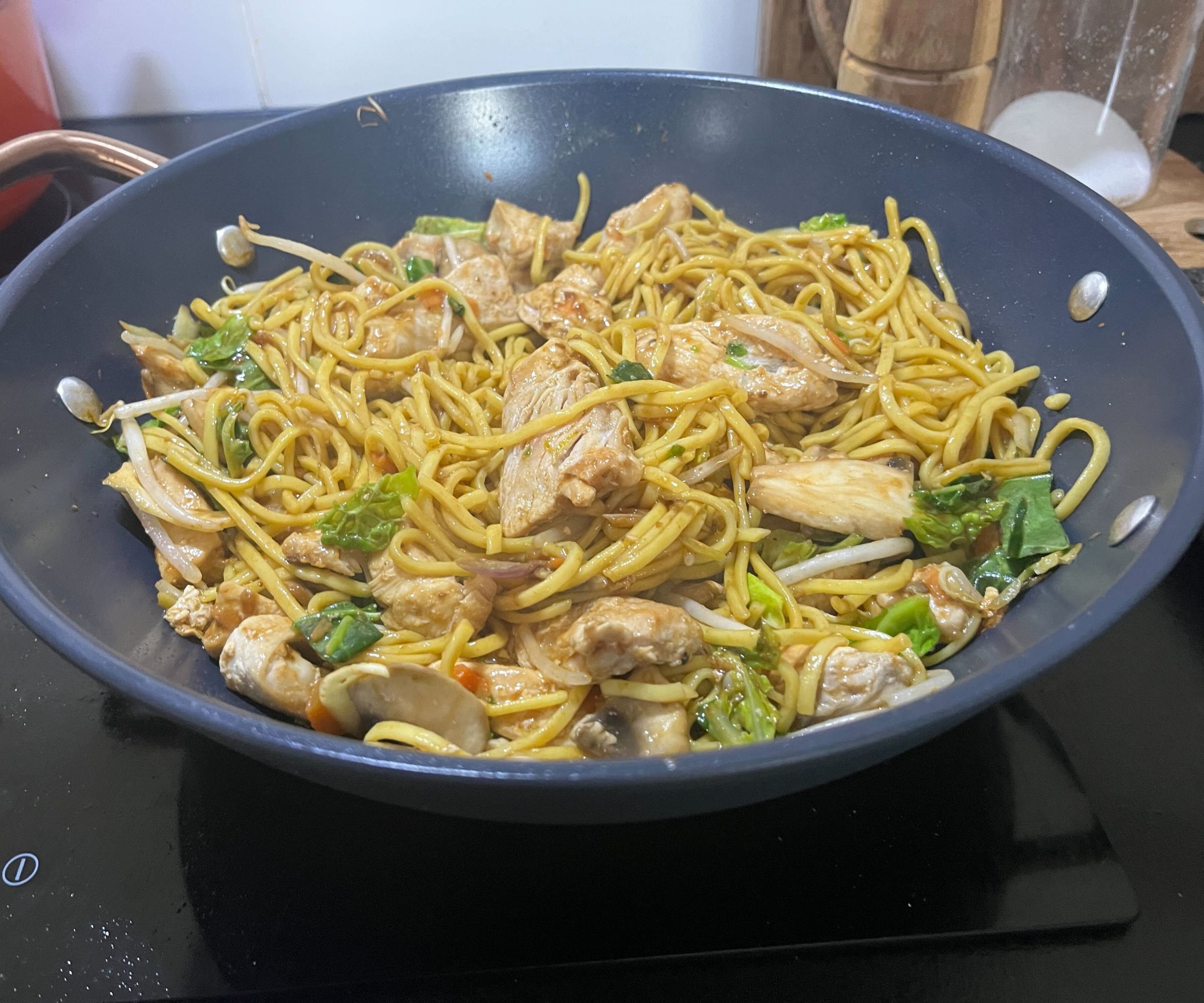 A chicken stir fry with egg noodles in a blue ceramic wok.