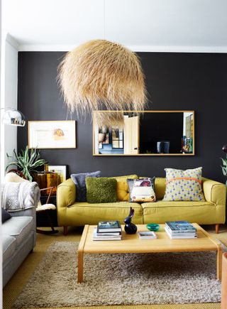 A dark modern grey living room with yellow sofa, seagrass ceiling pendant light and brass-framed rectangular mirror