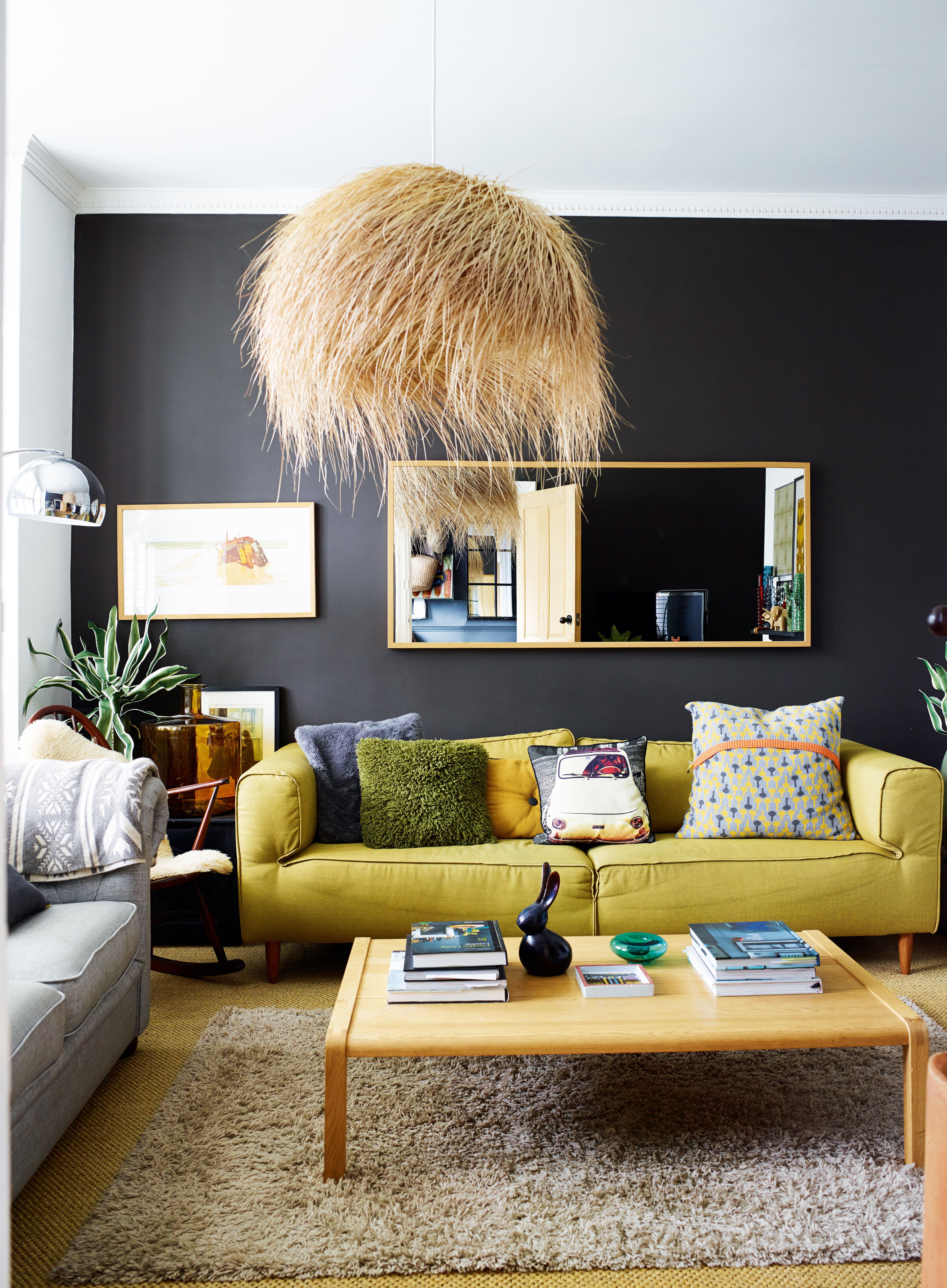 A dark modern grey living room with yellow sofa, seagrass ceiling pendant light and brass-framed rectangular mirror