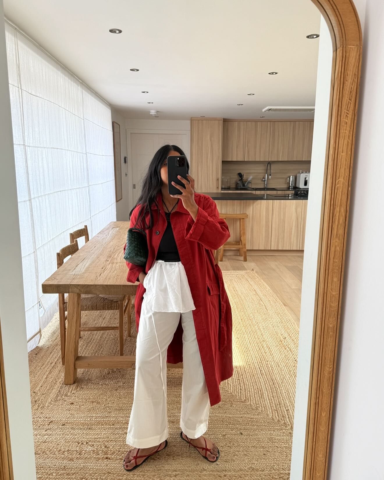 Monikh wears a red trench coat, white trousers, and red naked sandals.
