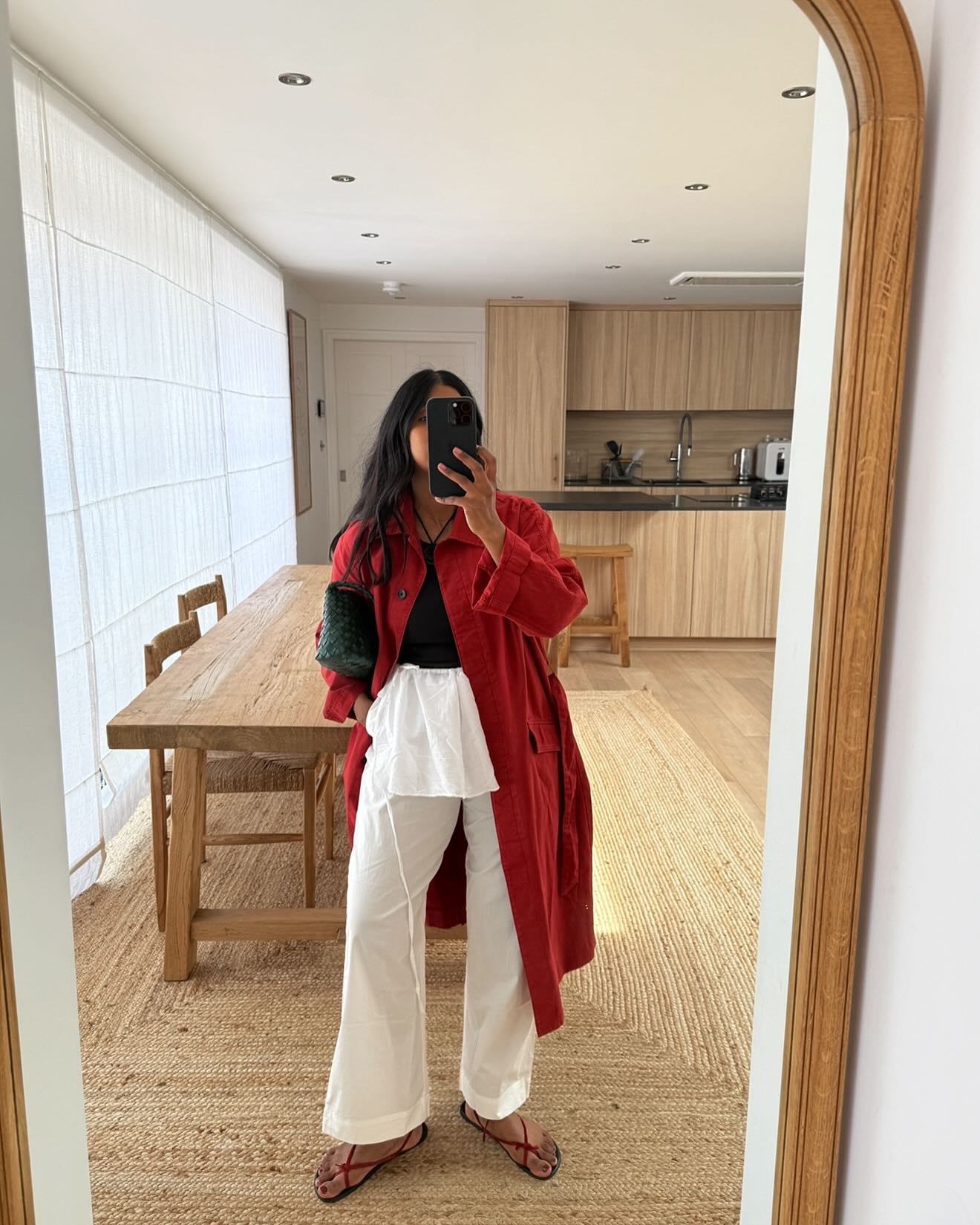 Monikh wears a red trench coat, white trousers, and red naked sandals.