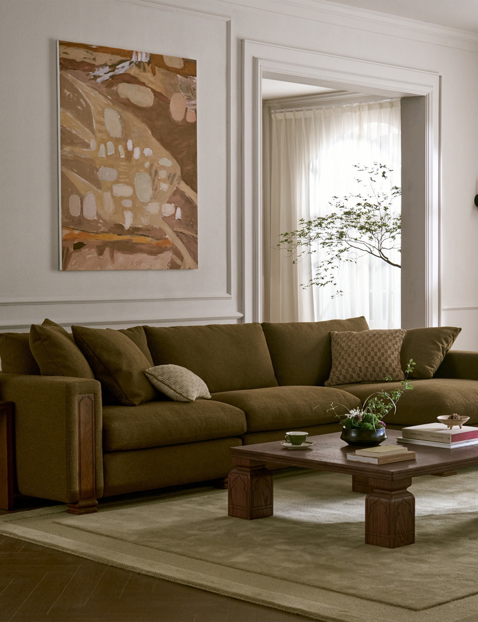 Serene living room featuring a moss green sectional couch, contemporary art, and a low-slung wooden coffee table