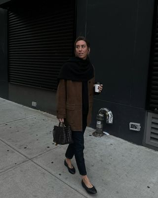 @hannahlewisstylist wearing black skinny jeans, a brown suede jacket, black top, a chunky knit scarf and ballet flats