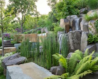 sloped garden with natural rock boulders, terraces, waterfall, ferns and grasses