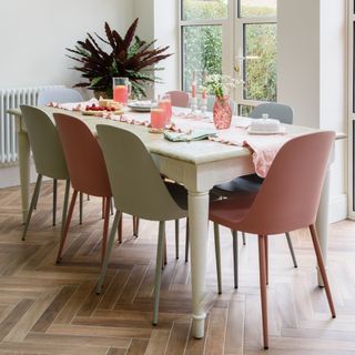 A dining room with a cream white table and contrasting chairs in pink and grey