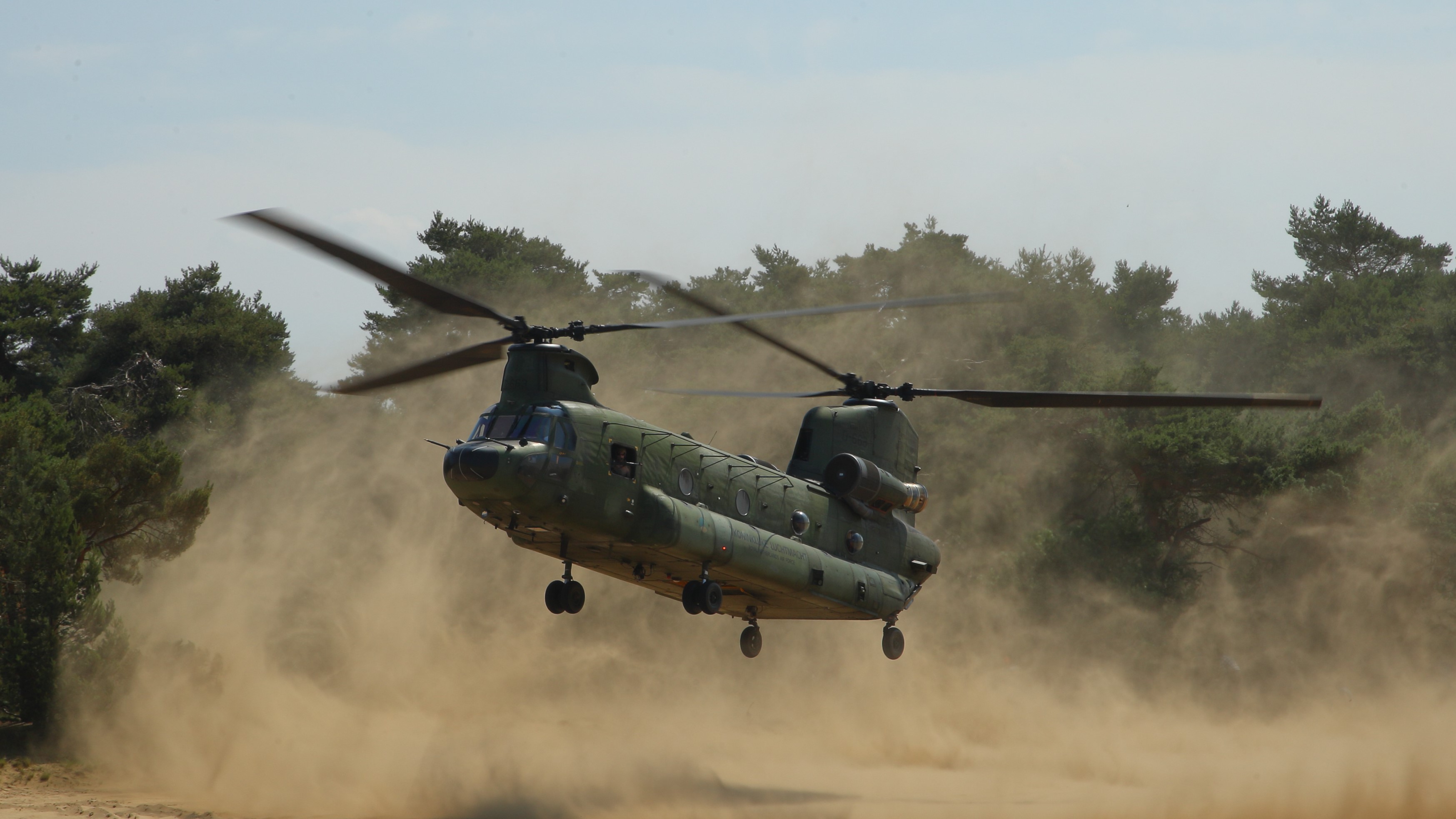 a chinook helicopter taking off in a dusty landscape with trees in the background