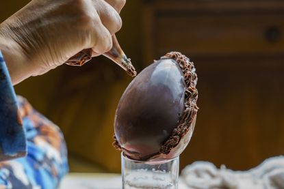 A homemade chocolate egg being hand decorated with chocolate buttercream frosting for Easter