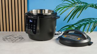 a black pressure cooker photographed against a blue background, showing its cooking presets, steam release valve, and Instant Pot branding