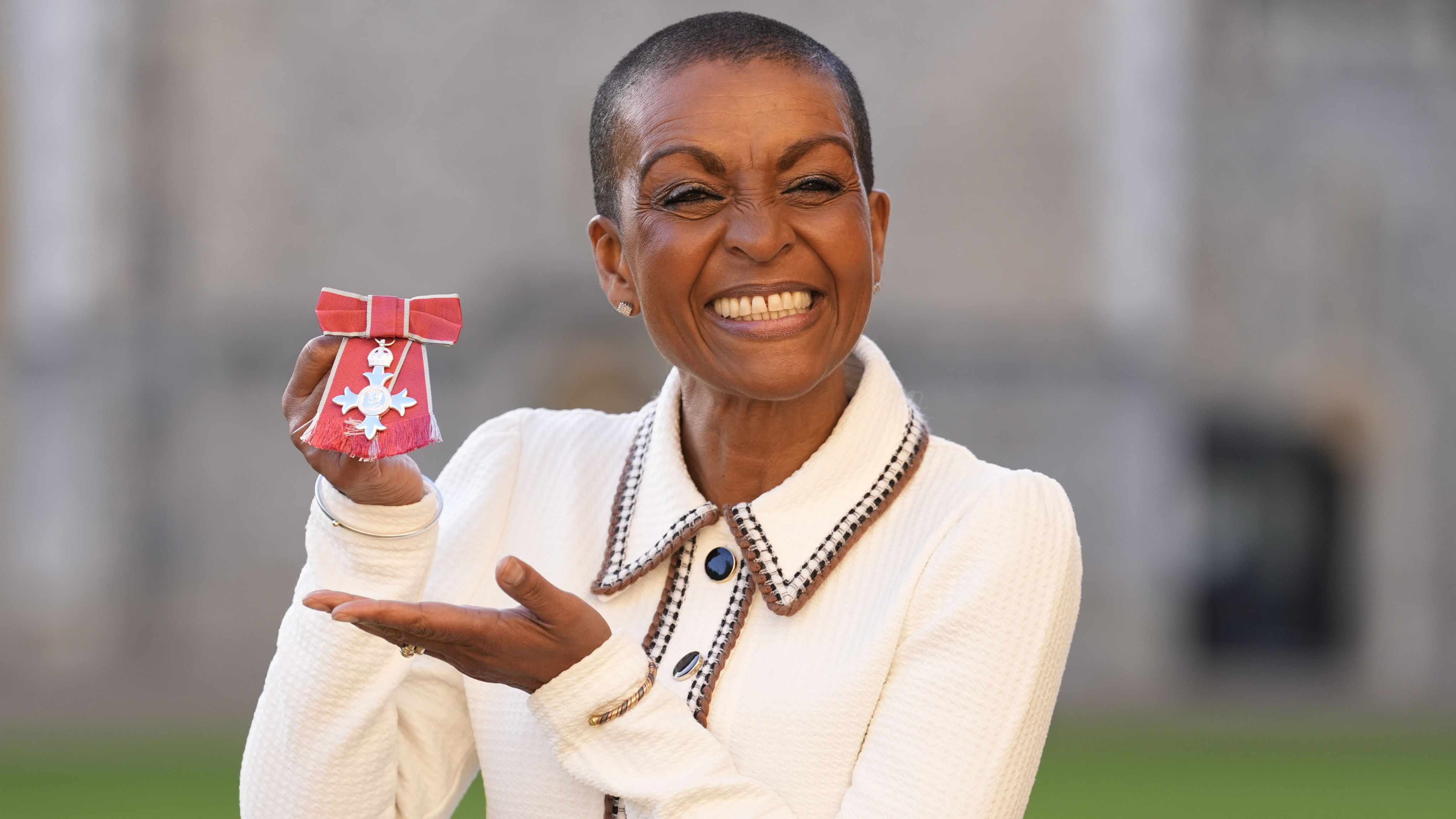 Adjoa Andoh beams and points to her medal after being made a Member of the Order of the British Empire (MBE)