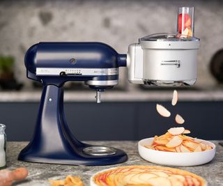 Kitchenaid food processor attachment slicing apples for an apple tart which is sat in front of a navy blue KitchenAid