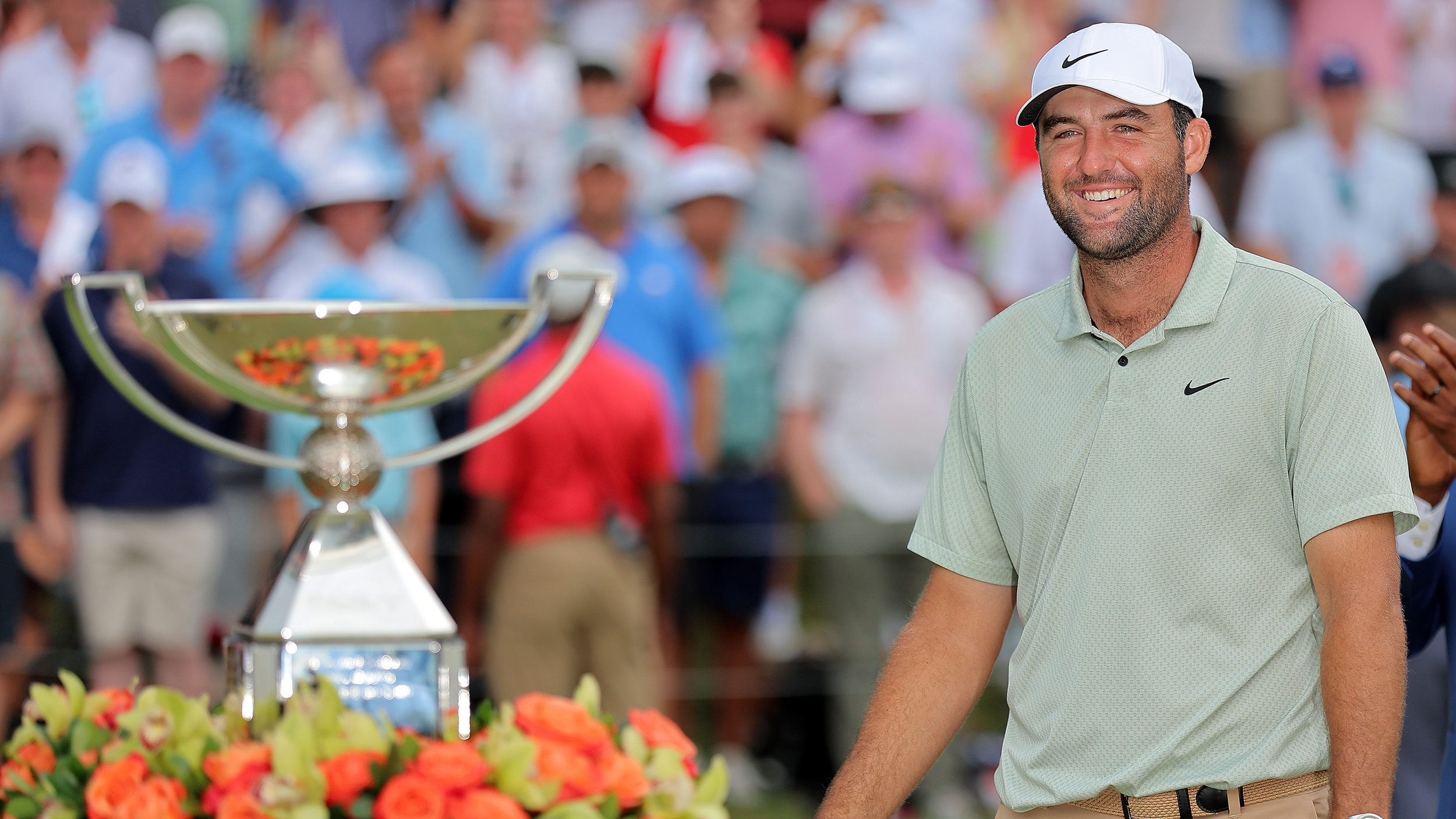 Scottie Scheffler smiles (right) with the FedEx Cup out of focus on the left