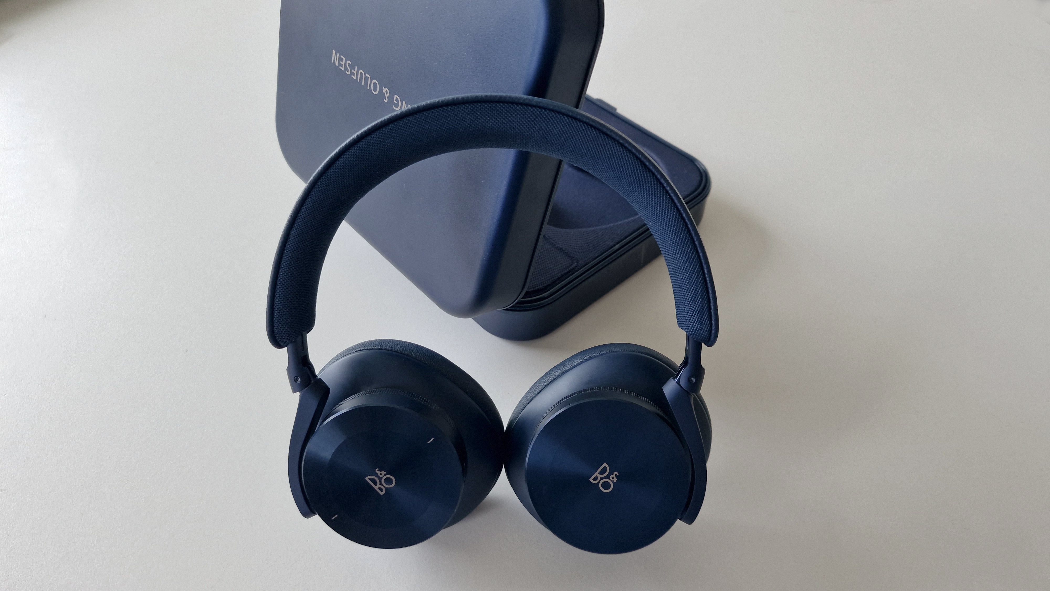 Beoplay H95 står lænet op ad det åbne etui på et hvidt bord