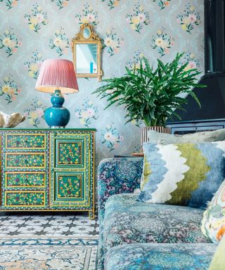 A colorful living room with blue floral wallpaper, a blue patterned couch and a painted green console table