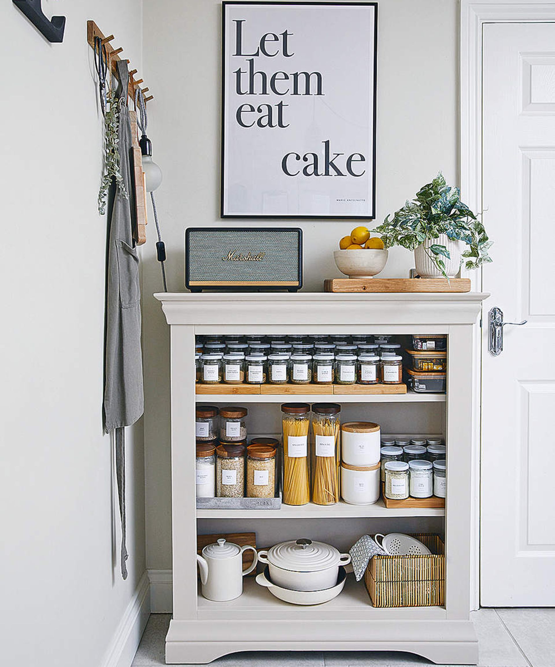 Dapur terbuka berisi makanan kering, termasuk pasta dan pilihan bumbu, dengan hiasan dinding berbingkai