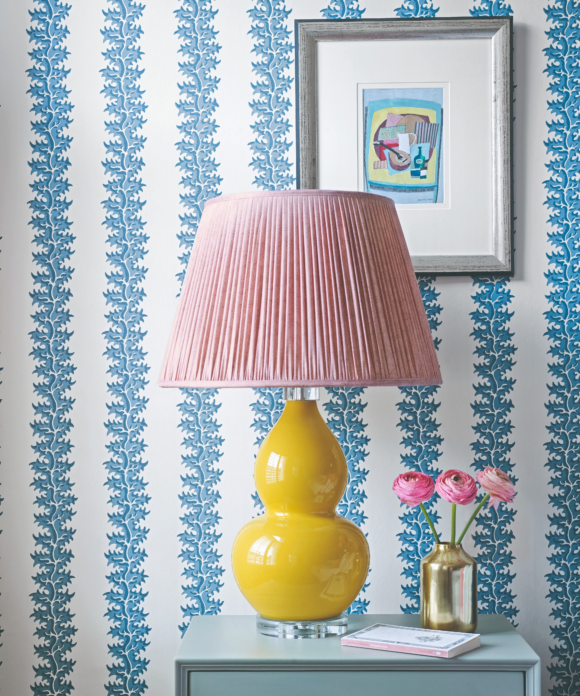 A bedroom with wall covered in striped white and blue wallpaper and a piece of art hung on the wall framed with an oversized white mount