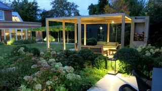 A pergola seating area with shrubbery and garden lighting designed by Charlotte Rowe