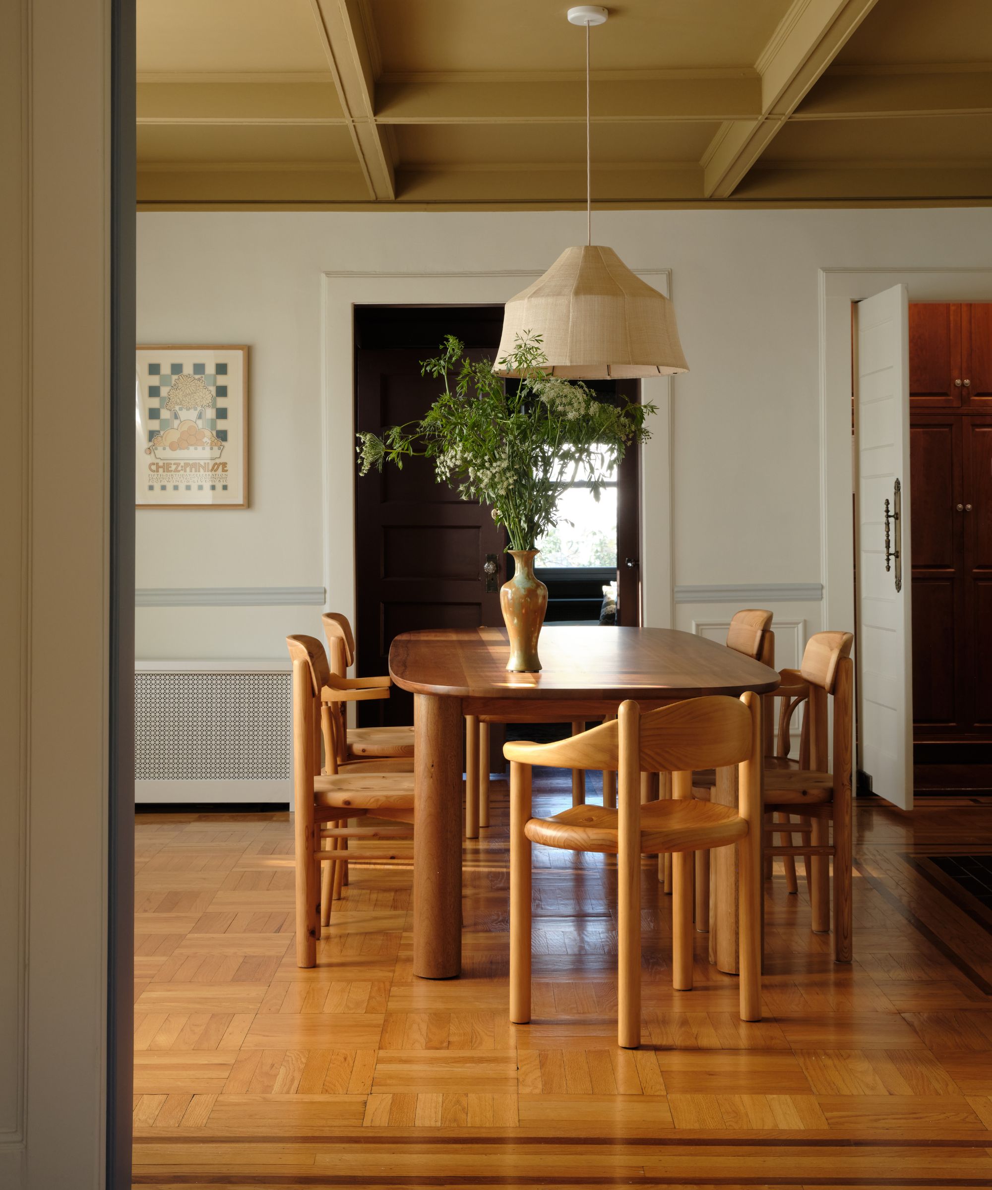 a serene white painted dining room with a painted wooden fireplace and a butter yellow accent ceiling with warm pine floors and table and chairs