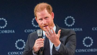 Prince Harry smiling and wearing a suit standing in front of blue background