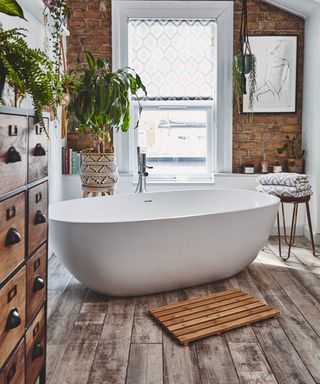 A bathroom with small white bath, wood effect flooring and exposed brick wall