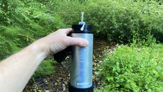 Hand holding blue LifeSaver Liberty Purifier in leafy woodlands