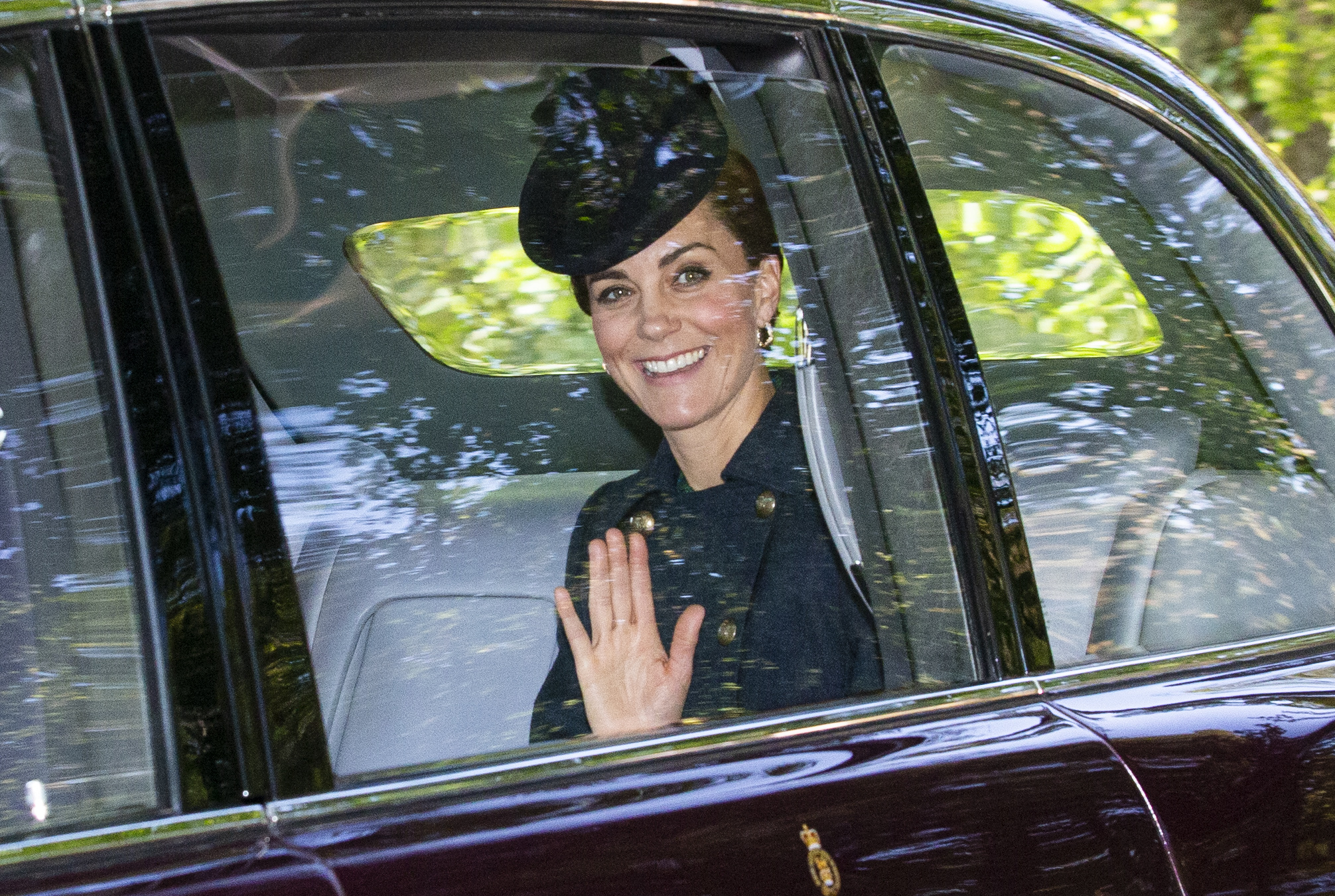 Princess Kate waving from a car in a coat and hat