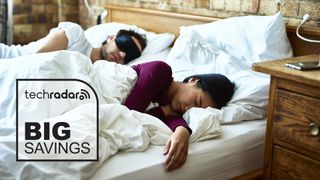 A couple sleep on a bed with a TechRadar deals logo