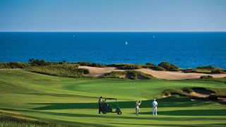 Golfers play a round at the Resort at Pelican Hill on a sunny day with blue skies and views of the Pacific Ocean
