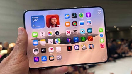 iPhone Duo opened and being held up by a single hand at a tech showcase.