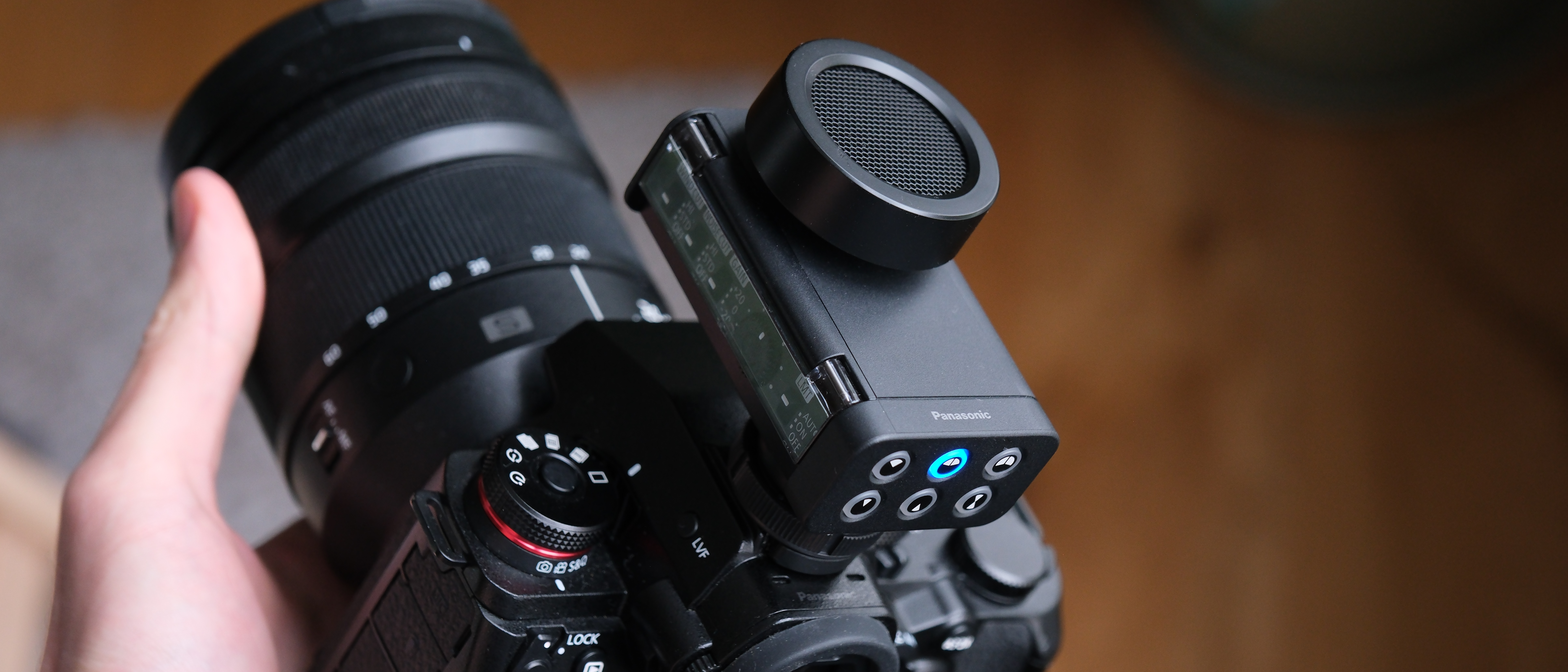 Panasonic Lumix DMW-DMS1 stereo microphone mounted on a Lumix mirrorless camera, showing the circular mic grille and top control buttons.