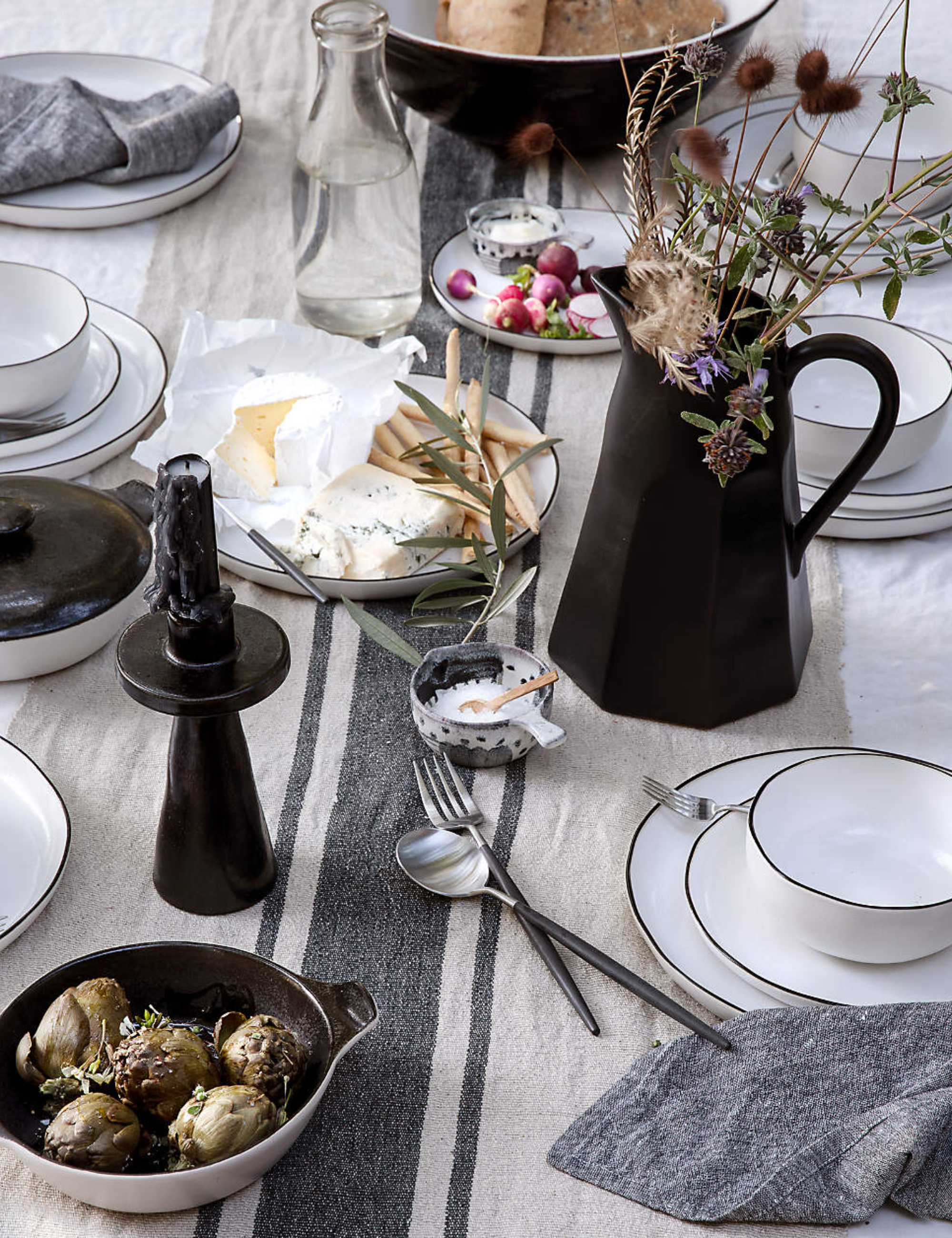 Black-and-white tablescape featuring stacked plates, striped table linens, and monochromatic pitchers