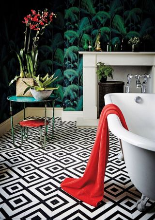 bathroom with monochrome patterned flooring, pattern clashing wallpaper, a freestanding bath and small side table with house plants