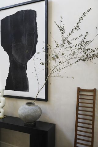 gray vase with single stem of dried eucalyptus on a black console, black and white artwork, small ladder, cream walls