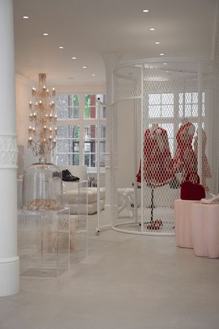 Three dresses on mannequins in an open, white metal cage next to a chandelier