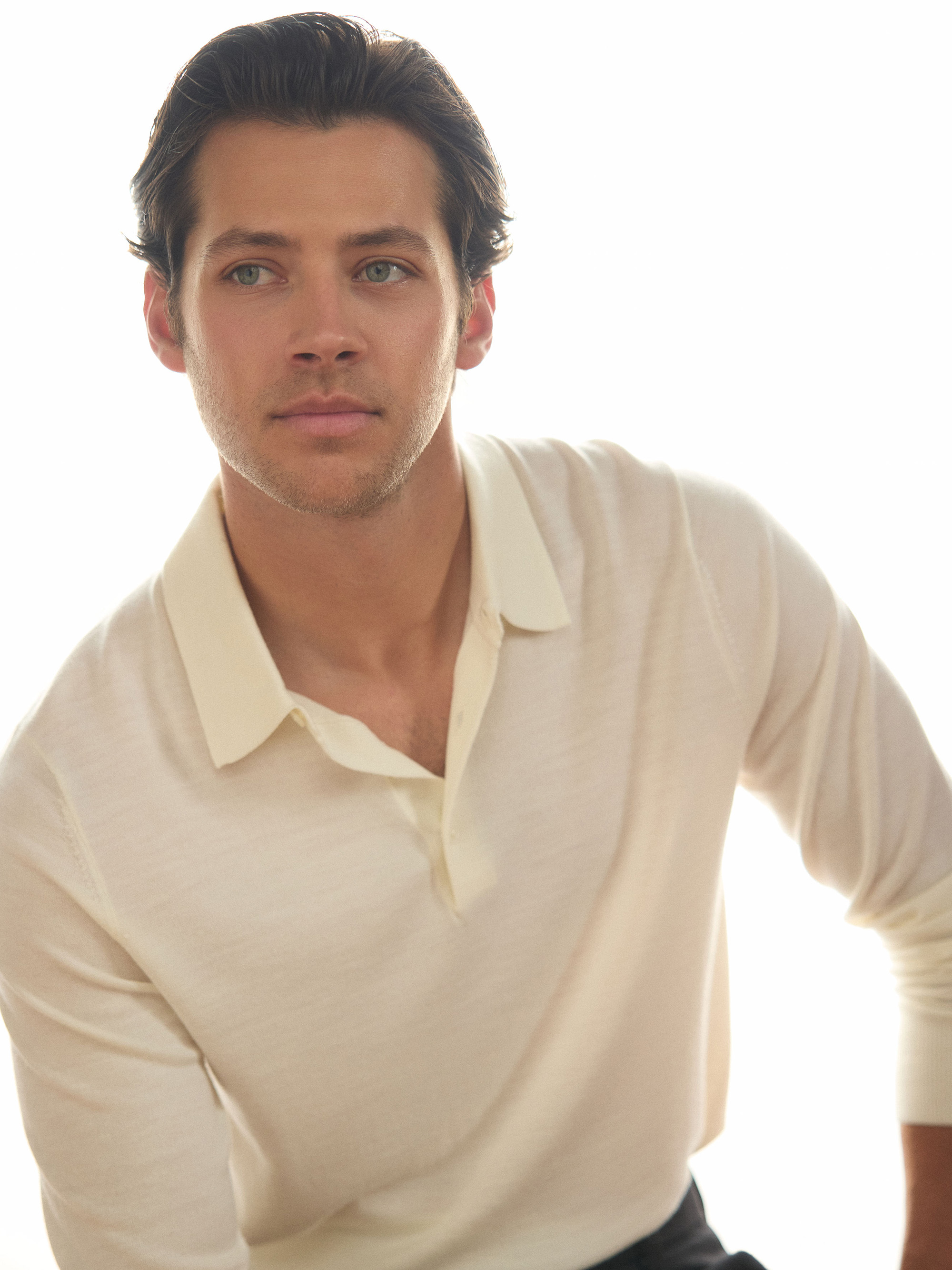 Matt Cornett photographed by Henry Wu and styled by Ashley Weston. Sitting in front of white background, he is wearing a white long-sleeve polo shirt.