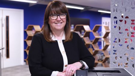 Julie Harrison, chief commercial officer (CCO) of Brother UK, pictured in an open plan office space leaning against a Brother printer.