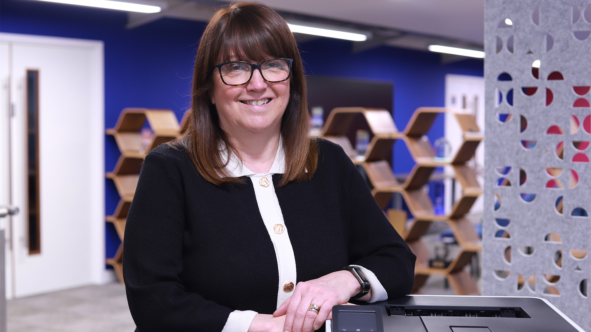 Julie Harrison, chief commercial officer (CCO) of Brother UK, pictured in an open plan office space leaning against a Brother printer.