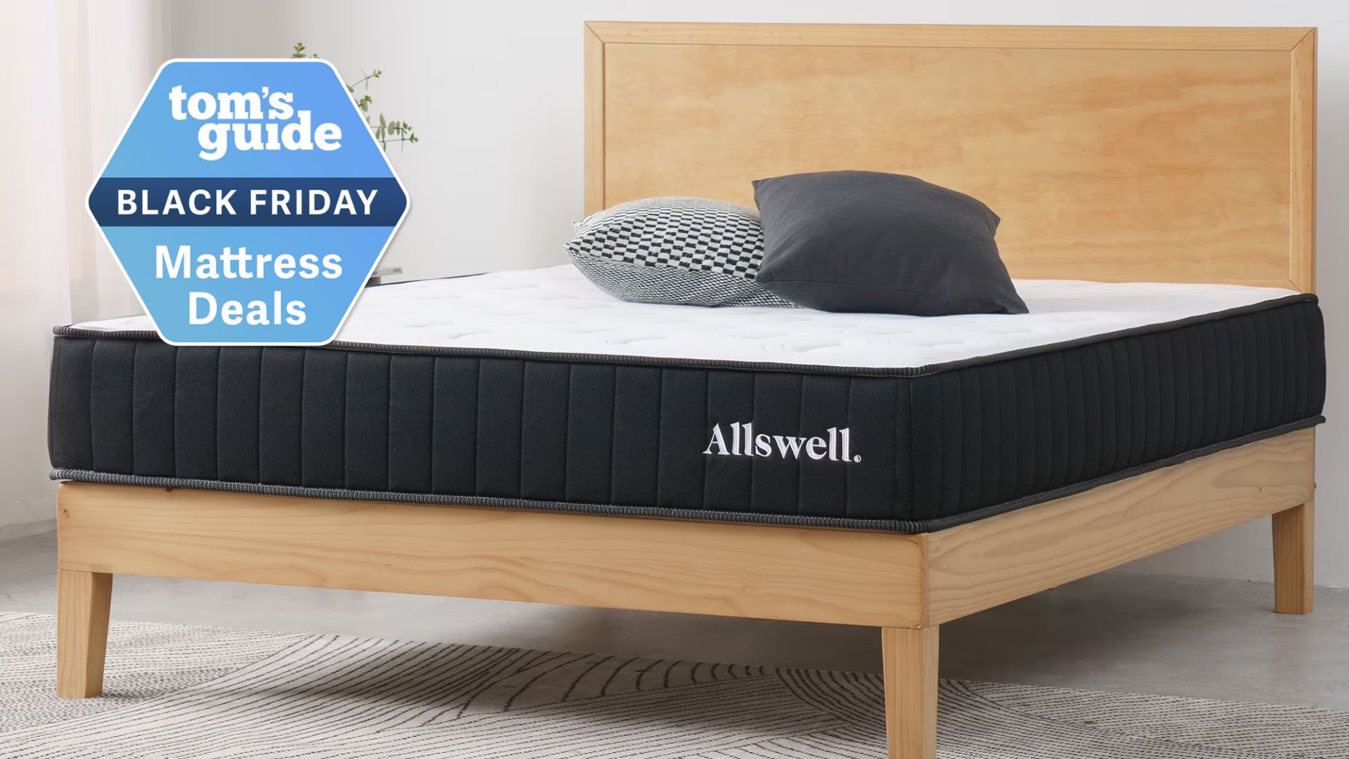 The image shows a mattress with a white cover and black sides placed on a wooden bed frame in a neutral bedroom. There&#039;s a badge laid over the image that says &#039;Tom&#039;s Guide Black Friday Mattress Deals&#039;