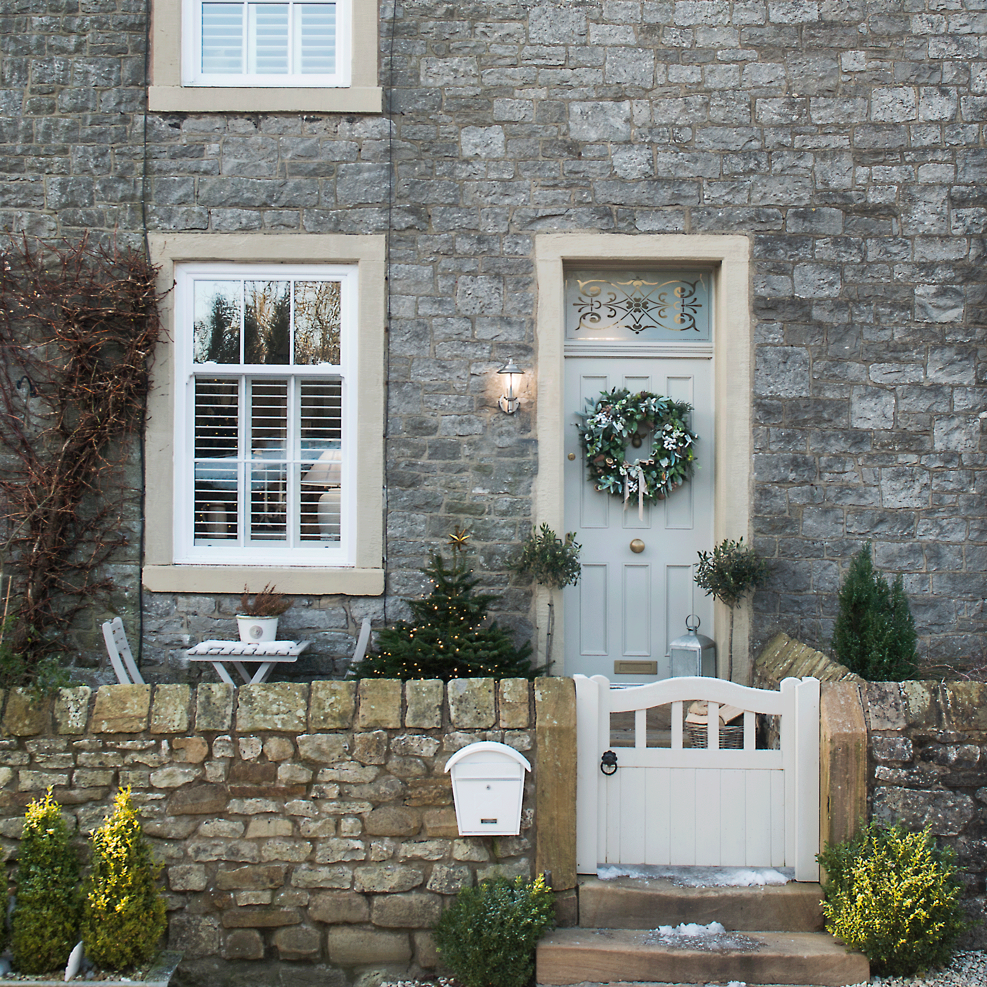 The front of a stone house with a pale blue door and a Christmas wreath and Christmas tree
