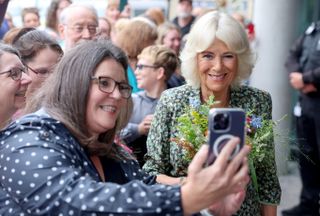 Queen Camilla poses for a selfie while wearing a floral dress at the Dyson Cancer Centre at Royal United Hospitals Bath NHS Foundation Trust on September 03, 2024