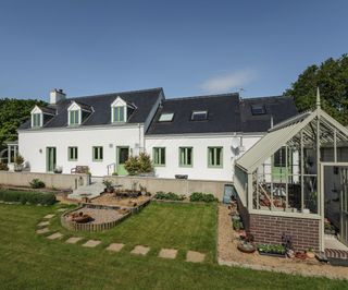 A large rendered home with bright green windows and doors and a greenhouse to the forefront