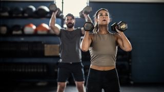 Woman in foreground and man in background working out with dumbbells