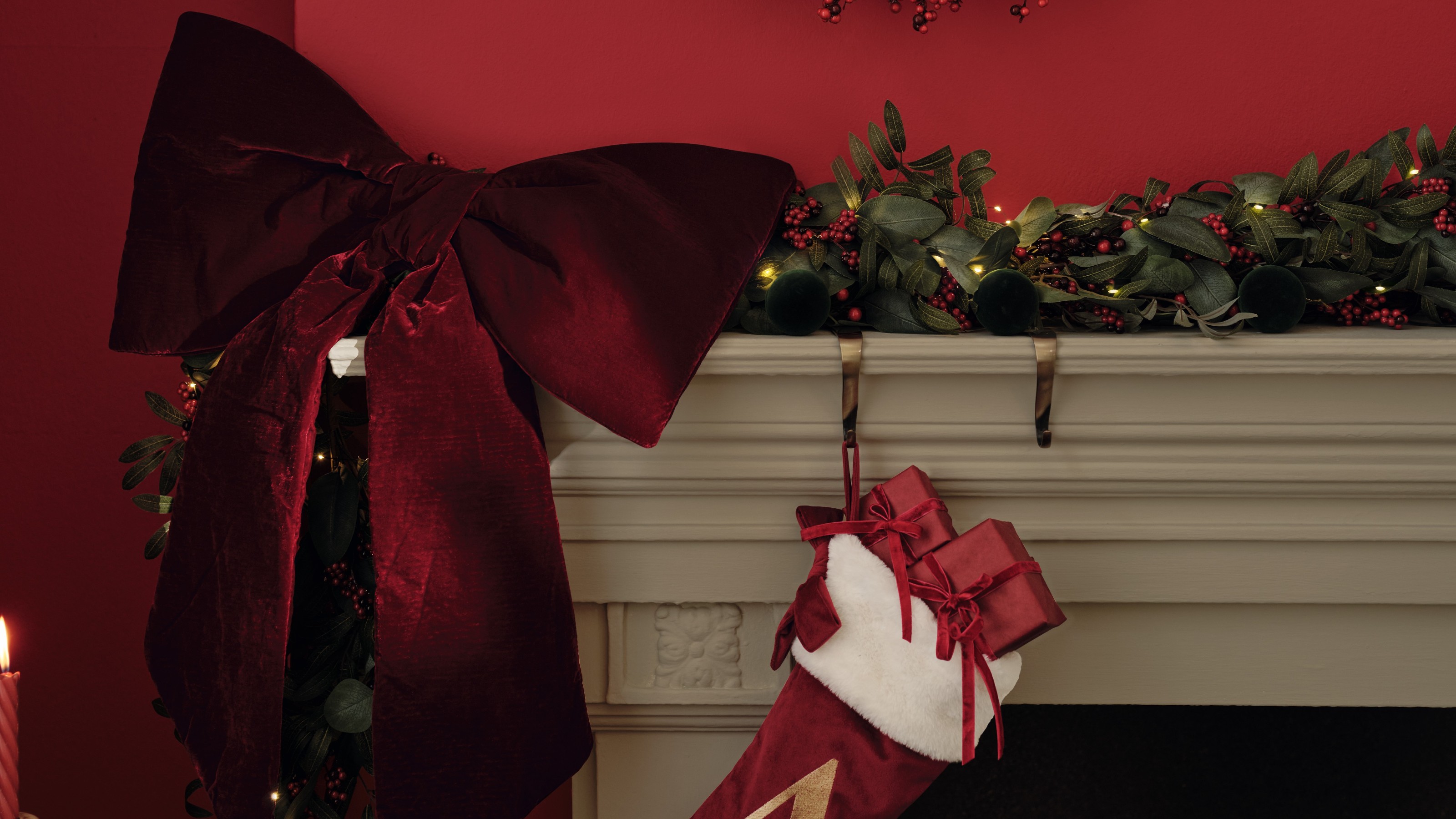 A mantelpiece decorated for Christmas with a garland, a stocking and the M&amp;S XL velvet bow in red
