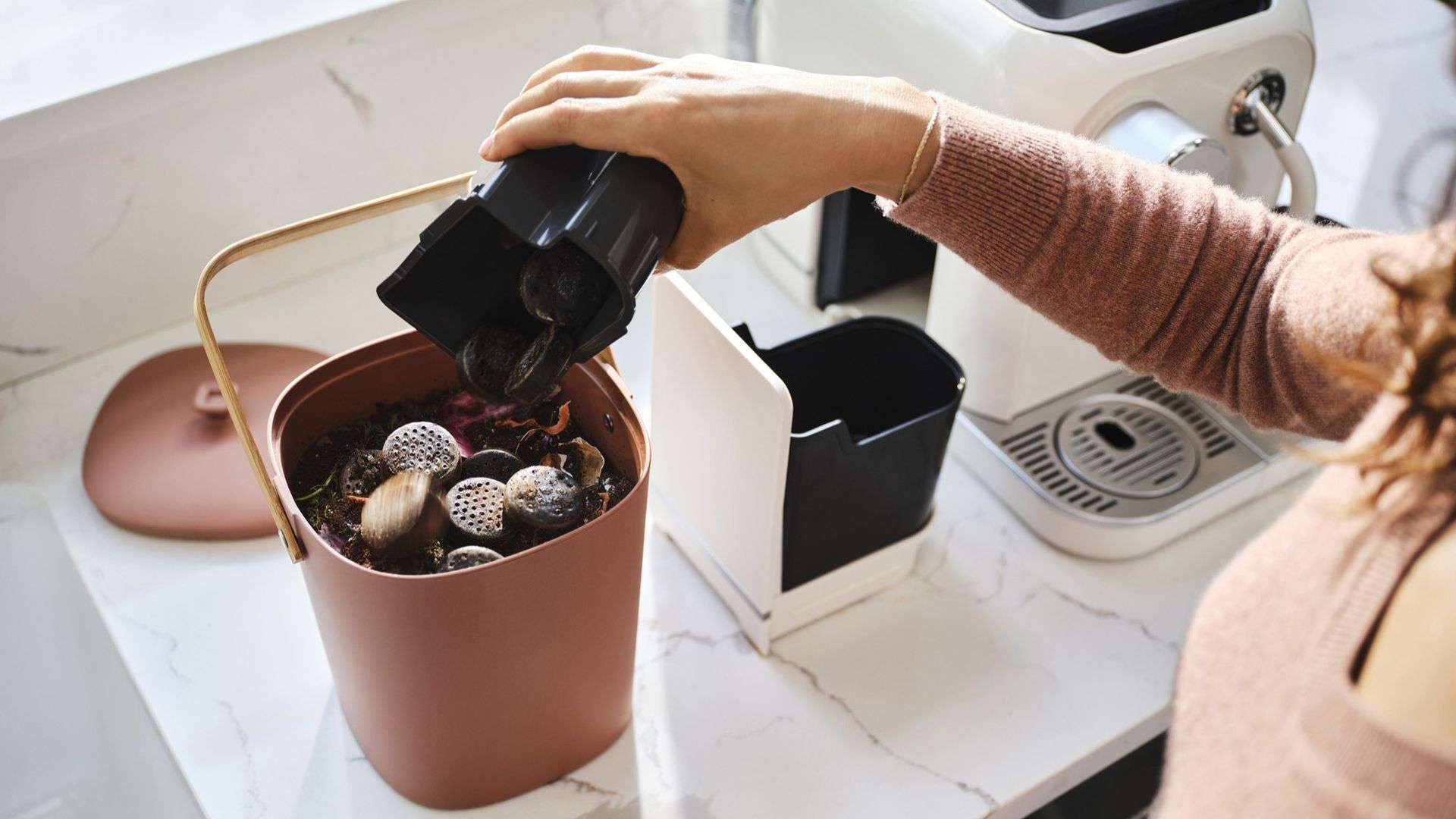 Woman tipping used pods from Keurig Alta coffee maker into food waste bin