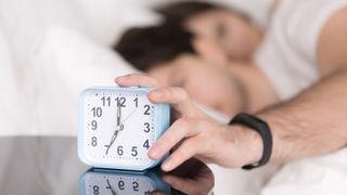 Man hitting alarm clock wearing fitness tracker