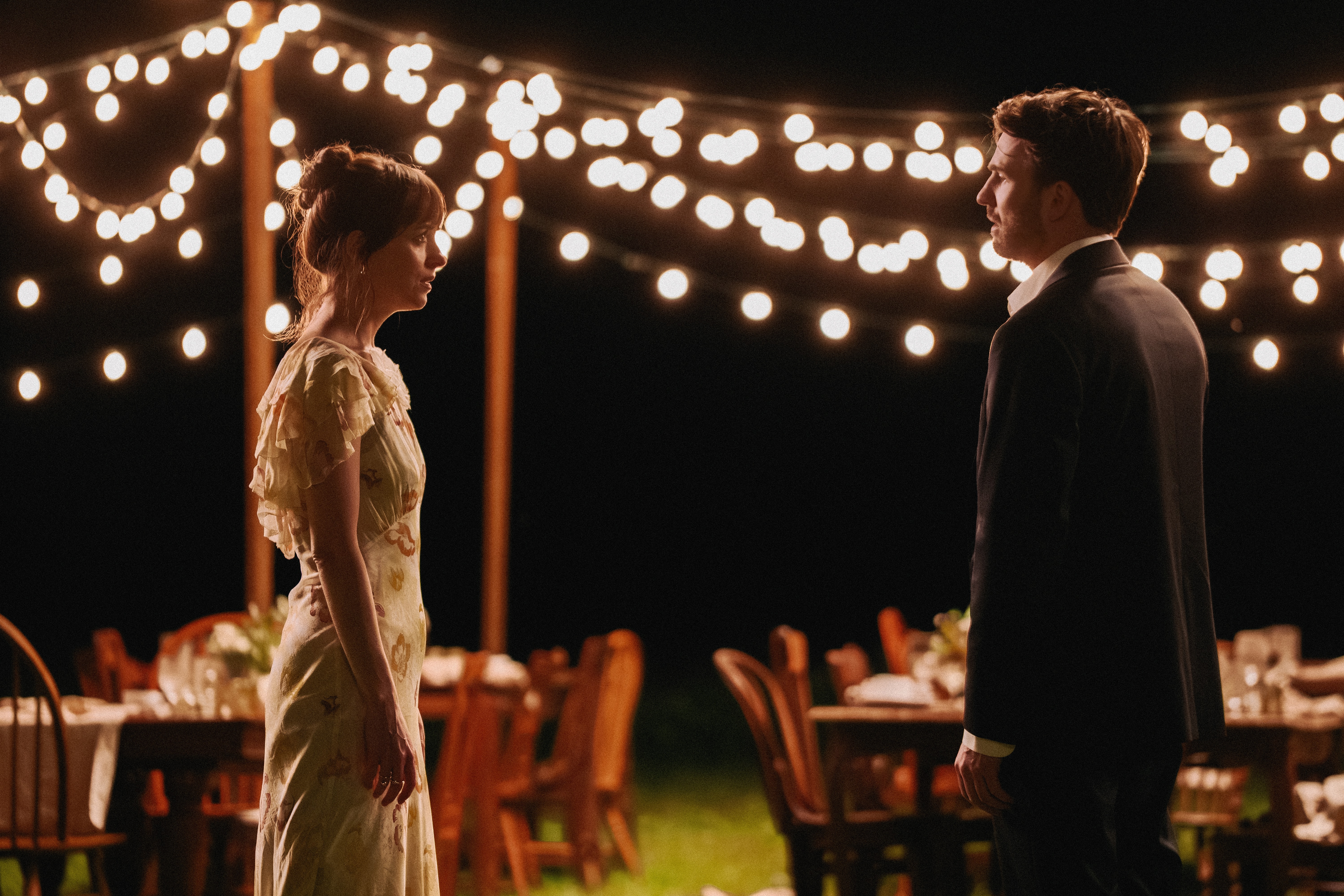 dakota johnson and chris evans having a conversation at an outdoor wedding in a still from the movie materialists